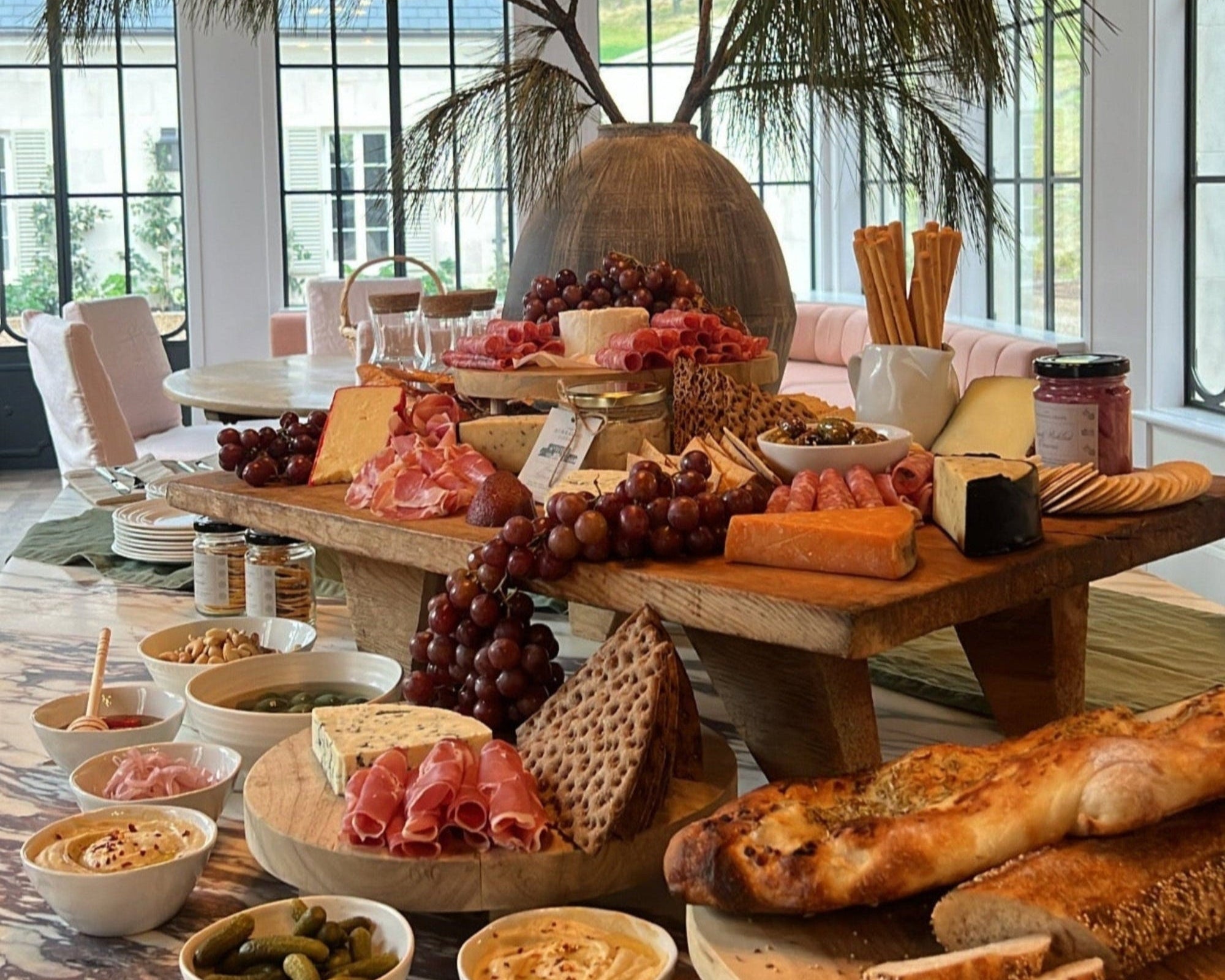 Gourmet platter with various foods including bread, cheese, and fruits in a modern interior setting.